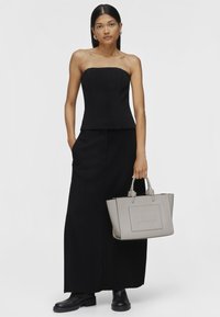 Haut noir sans bretelles au design ajusté, associé à une jupe maxi noire. Tiens un sac fourre-tout en cuir gris avec un détail en relief "TOUS". Bottines noires.