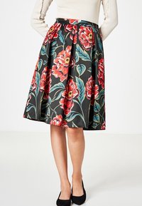 Jupe A-line florale avec de grandes fleurs rouges et roses sur un fond noir, dotée d'une taille ajustée et d'un design plissé.