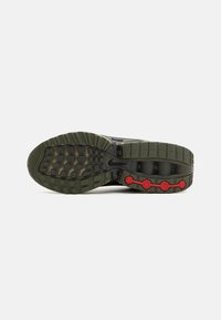 Nike sporta apavu zole ar olīvu zaļu gumijas apakšu, teksturētu saķeres rakstu un sarkaniem akcentiem tuvāk papēdim.