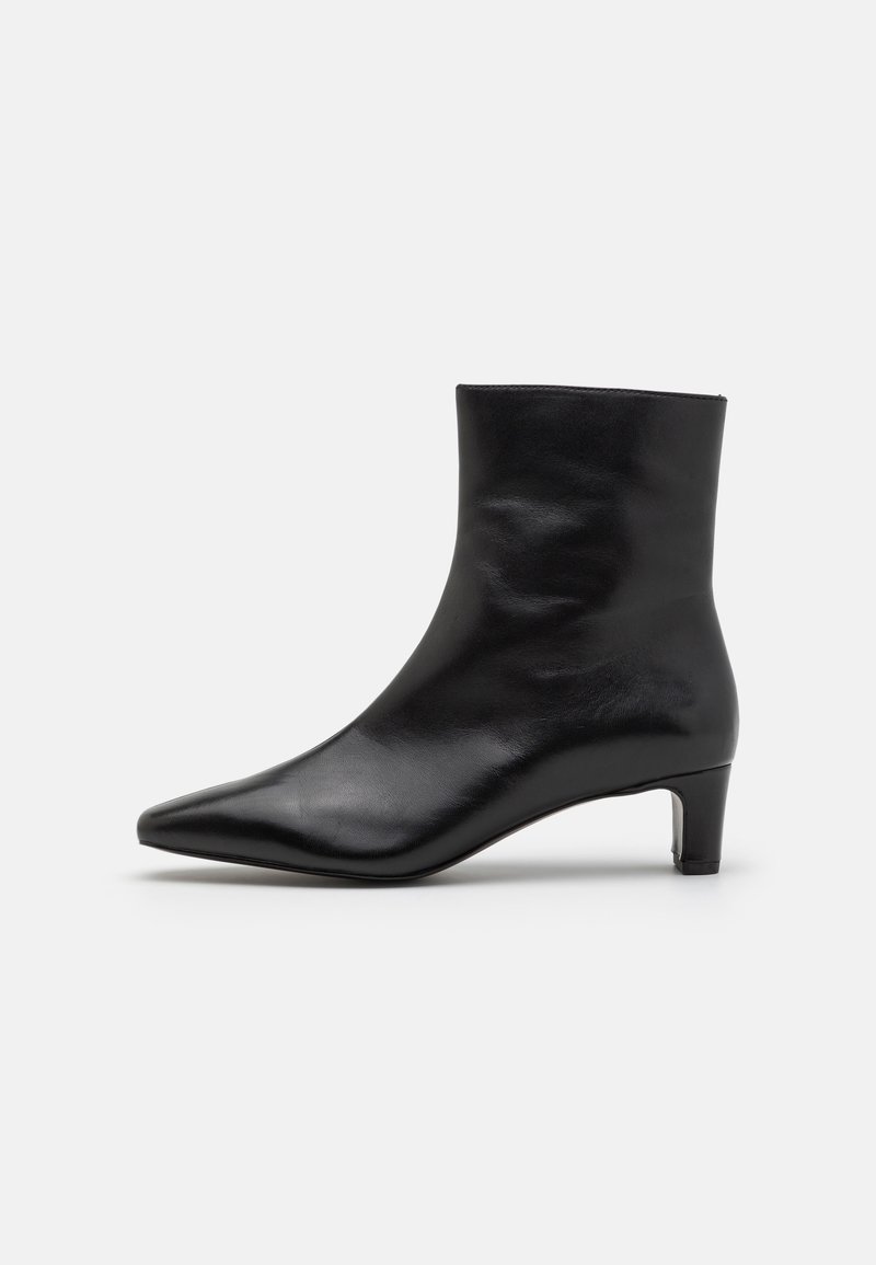 Bottine en cuir noir avec bout pointu et petit talon kitten, présentée sur un fond gris uni.