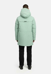 Mięta zielona parka ocieplana z kapturem, z tylnym wentylkiem i czarnymi akcentami. Połączona z czarnymi spodniami i butami. Gładka faktura.