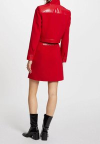 Rød cropped jakke med skinnende teksturerede skuldre, matchende rød nederdel og knæhøje sorte patenterede læderstøvler. Rent design og tætsiddende form.