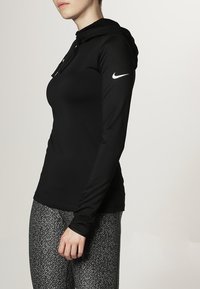 Sudadera negra de manga larga con un diseño ajustado, hecha de tela suave. Cuenta con un cordón y un logotipo discreto en el hombro izquierdo.