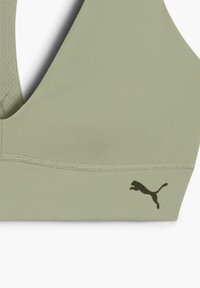 Svijetlozeleni sportski grudnjak izrađen od glatke tkanine. Ima dizajn s V-izrezom i crni Puma logo sa strane, dok se na leđima nalazi teksturirani panel.
