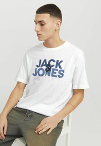 Hvid bomulds T-shirt med fed marineblå tekst, der står "JACK & JONES." Korte ærmer og rund halsudskæring.