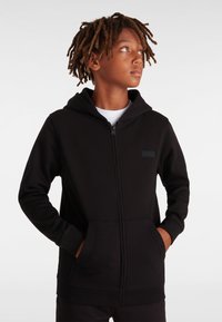 Svart zip-up huvtröja i mjukt tyg, med en känguruficka, ribbade ärmslut och en liten svart logotyp på bröstet.