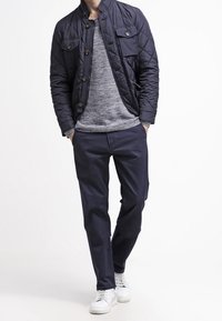 Granatowa pikowana kurtka z zatrzaskami i kieszeniami na piersi, pod spodem szary sweter dziany, do tego granatowe spodnie i białe trampki.