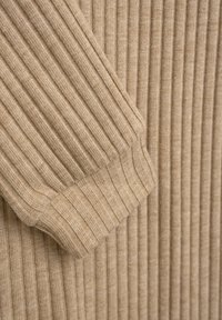 Beiger, gerippter Stoff, der eine Nahaufnahme des Bündchens eines Pullovers zeigt, mit vertikalen Streifen und einer gestrickten Textur. Feine Lichtfasern sind sichtbar.