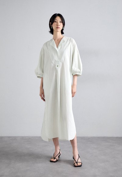 Weiß und grün gestreiftes Kleid mit Kragen, puffärmeligen Ärmeln und taillierter Taille. Kombiniert mit schwarzen Riemchensandalen und minimalistischem Schmuck.