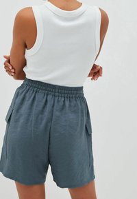 Biały, bezrękawnik z prążkowanego materiału, zestawiony z luźnymi, łupkowoniebieskimi szortami z elastycznym pasem i kieszeniami po bokach.