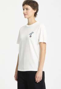 Hvid kortærmet t-shirt i bomuld med rund halsudskæring, med et flerfarvet broderet design på venstre brystområde.