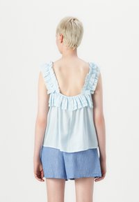 Lichtblauw rugloos topje met rimpelige schouderbanden, gelaagde rimpeldetails bij de halslijn, gecombineerd met blauw-wit gestreepte shorts.