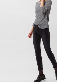 Svarta denimjeans i kombination med en mönstrad långärmad skjorta. Skjortan har ett litet monokromt tryck och har en avslappnad passform.