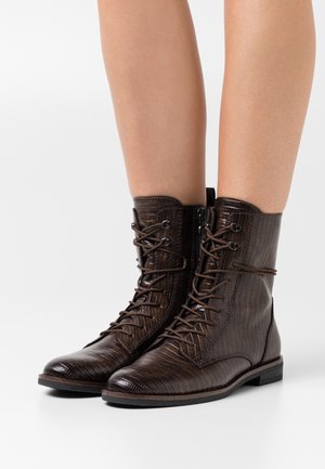 Bruna texturerade läderanklar med snörning fram, rund tå och platt sula. Har subtilt präglat mönster och metallhål.