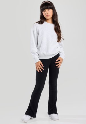 Grauer Sweatshirt mit langen Ärmeln, kombiniert mit schwarzen gerippten Schlaghosen. Das Model trägt weiße Turnschuhe und ein passendes Haarband. Schlichter Hintergrund.