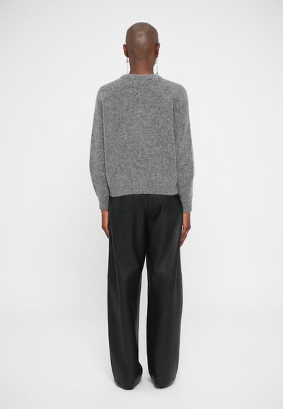 Maglione grigio tessuto con maniche lunghe e orlo a costine, abbinato a pantaloni neri larghi. L'outfit è visto da dietro.
