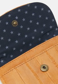 Innenseite einer tan-farbenen Lederbrieftasche mit einem marineblauen Stofffutter, das mit weißen Sternmustern verziert ist, gesichert mit einem dekorativen Messing-Druckknopf.