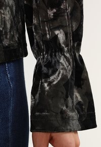 Black velvet shirt featuring a floral pattern with a gathered, flared sleeve. The texture is soft, and the fabric has a slight shine.