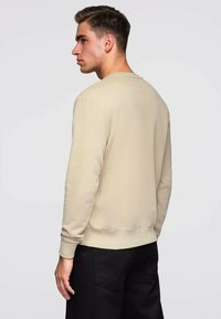 Beige sweatshirt met een eenvoudig ontwerp, ronde hals, geribbelde manchetten en zoom. Achteraanzicht toont een gladde textuur en minimale details.