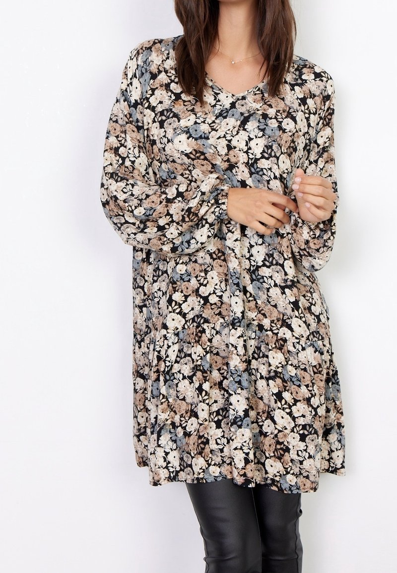 Robe tunique florale avec manches longues, décolleté en V, fond noir, et un mélange de fleurs beiges, bleues et blanches ; tissu léger.