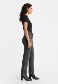 Camiseta negra de canalé combinada con jeans de talle alto grises y botas de ante negras con tacón, que destacan un diseño ajustado y una tela texturada.