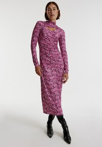 Rosa Blumen-Maxikleid mit langen Ärmeln, hohem Kragen und Ausschnitt-Details, das eine taillierte Silhouette und eine weiche Stofftextur aufweist. Kombiniert mit glänzenden schwarzen Stiefeln.