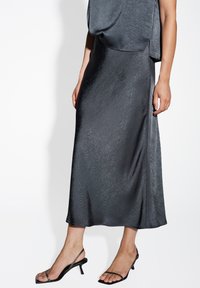 Zijdeachtige zwarte rok met een gestructureerde afwerking, vloeiende design, middenkuitlengte, gecombineerd met zwarte strappy hakken met een lage hak.