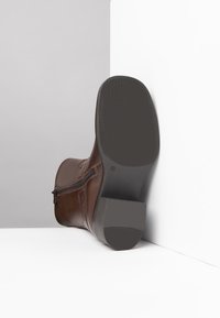 Bruine leren laars met een ritssluiting, rechthoekige hak, platte zool en een gestructureerde buitenzool. Het bovenwerk heeft subtiele stikdetails.