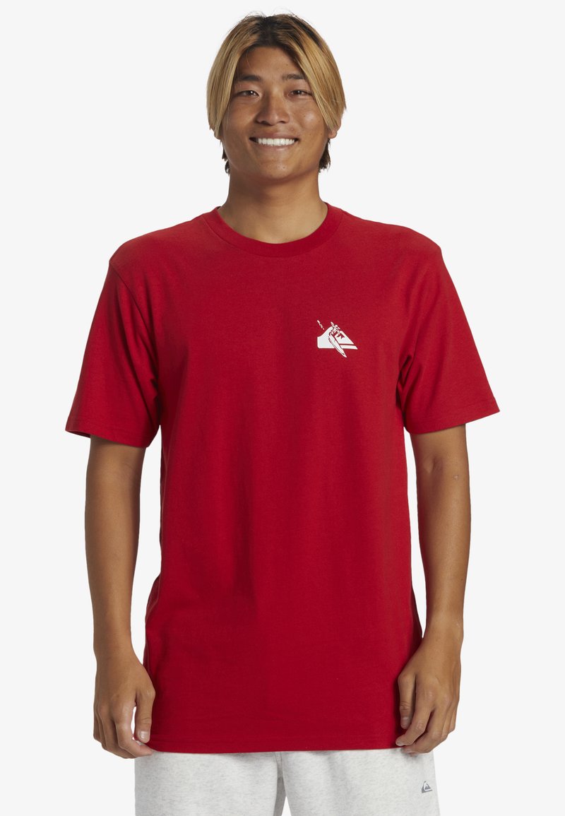 Camiseta de algodón roja con cuello redondo, que presenta un pequeño diseño gráfico blanco en la parte superior izquierda del pecho. Manga corta y corte relajado.