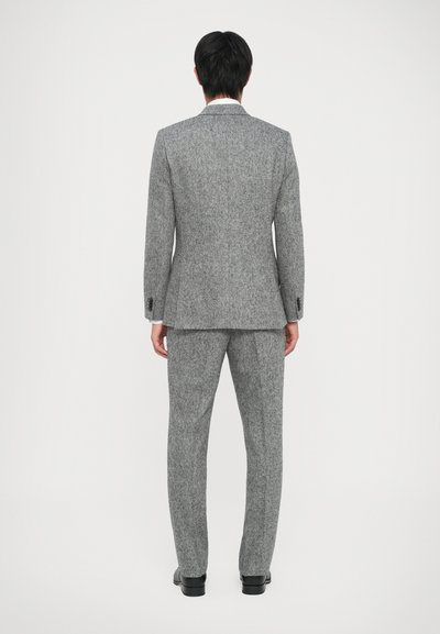 Grauer Tweed-Anzug mit schmaler Passform. Die Jacke hat einen mittigen Schlitz und Reverskragen. Die Hose ist gerade geschnitten und verfügt über Gürtelschlaufen.