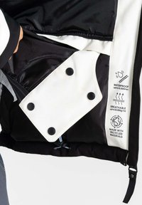 Wasserdichte Jacke in Schwarz und Weiß, Innenansicht mit einer Reißverschlusstasche, schwarzen Druckknöpfen und Pflegeetiketten, die atmungsaktive und recycelte Materialien angeben.