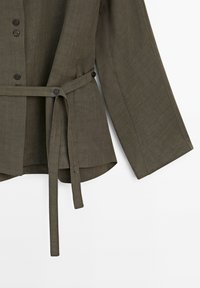 Olijfgroen linnen overhemd met lange mouwen, vooraan knopen en een stoffen riem die om de taille is gestrikt, getoond op een witte achtergrond.