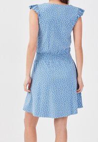 Blaues Kleid mit weißen Punkten, kurzen Rüscheärmeln, elastischem Bund und einem ausgestellten Rock, der weiße Punkte auf einem einfarbigen blauen Hintergrund zeigt.
