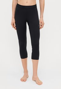 Leggings capri pretos feitos de um tecido elástico com uma cintura alta apresentando a marca "PeakPerformance". Leves e com uma textura suave.