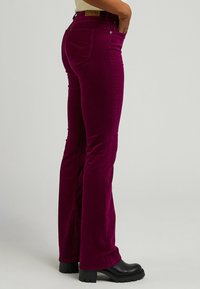 Getailleerde fluwelen flared broeken in diep magenta met een gestructureerd oppervlak, twee achterzakken en een hoge taille, gecombineerd met zwarte platformlaarzen.