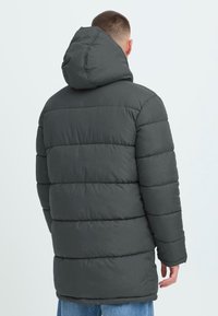 Mørk grå pufferjakke med hætte, quiltet design og ribbede manchetter. Har en mellemlang pasform og let, syntetisk materiale.