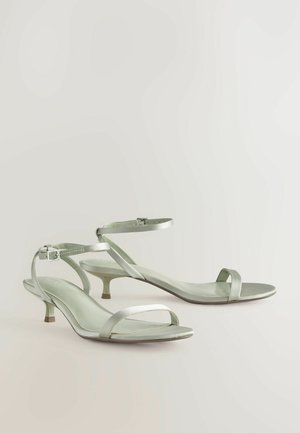 Sandali con tacco in satin verde chiaro, dotati di una sottile cintura alla caviglia, punta aperta e un elegante tacco a kitten, con un design minimalista.