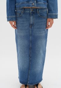 Denim maksi suknja svijetloplave boje, s ravnim siluetom, prednjim dugmadi za zatvaranje i džepovima, s izblijedjelom teksturom i detaljima šivanja.