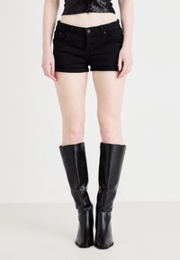 Shorts de mezclilla negros con un ajuste slim y diseño de bolsillos estándar, combinados con botas de cuero negro brillantes hasta la rodilla y con punta afilada.