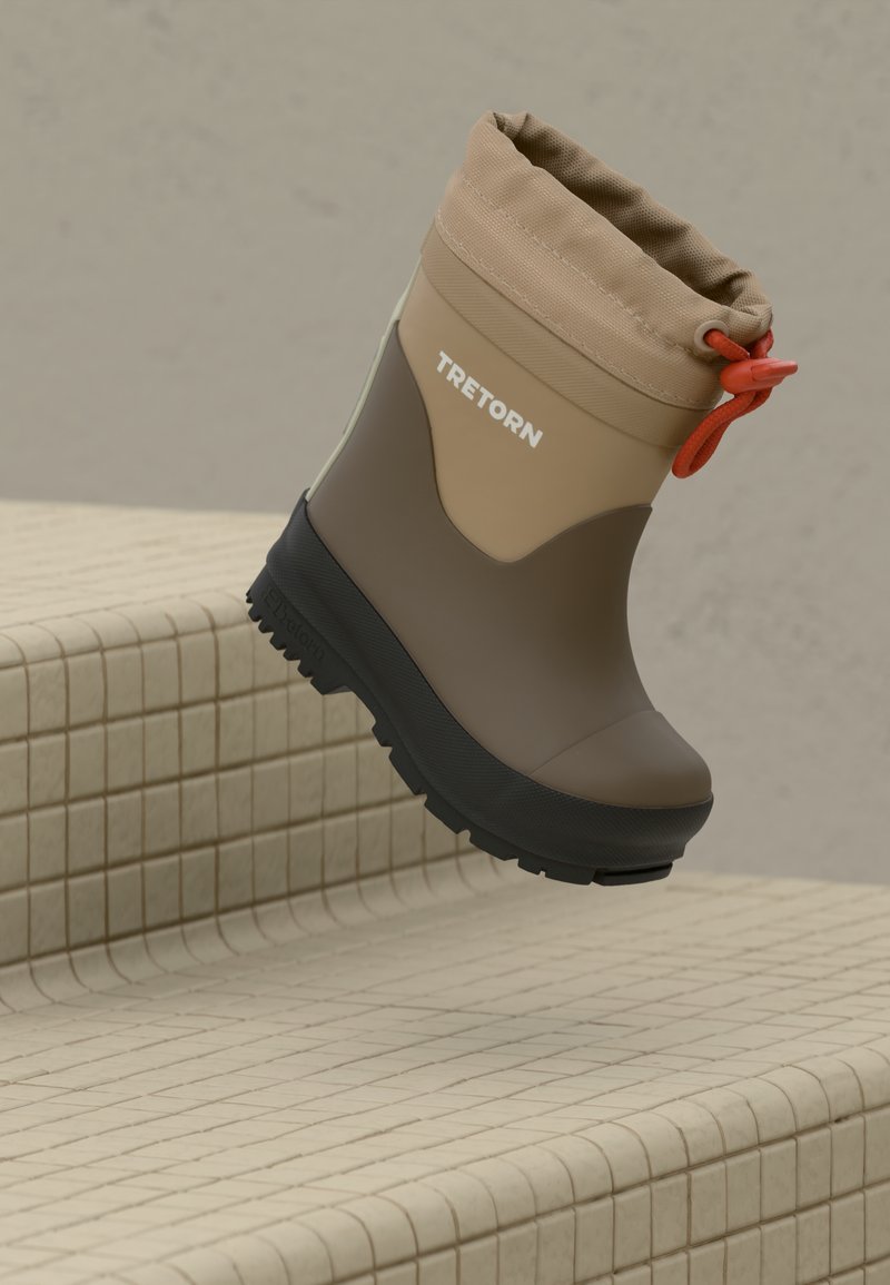 Bottes étanches Tretorn marron et beige avec semelle noire et cordon orange, placées sur une surface carrelée beige.