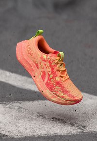 Baskets de course orange vif avec un dessus texturé, des accents jaunes et une semelle rembourrée. Comprend un logo prominent et des lacets contrastants.
