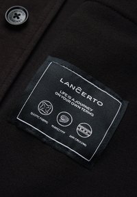 Czarna metka z białym przeszyciem. Tekst zawiera "LANCERTO" oraz symbole dla elastycznej tkaniny, idealnego dopasowania i właściwości przeciwgnieceniu.