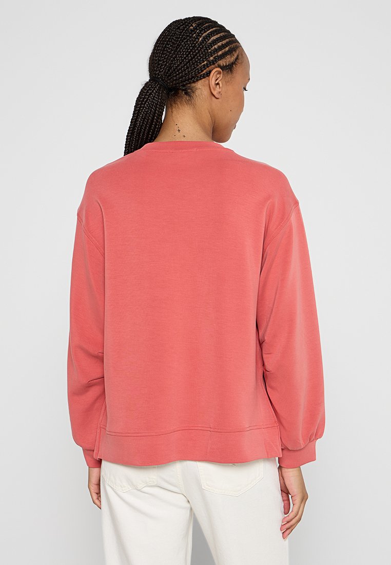 Korallenfarbener Sweatshirt aus weichem Stoff, mit lockerem Schnitt, langen Ärmeln und einem leicht verkürzten Saum. Keine Muster oder auffälligen Hardware-Elemente sichtbar.
