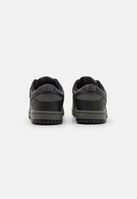 Un par de zapatillas Nike en negro y gris oscuro se muestran desde atrás sobre un fondo blanco.