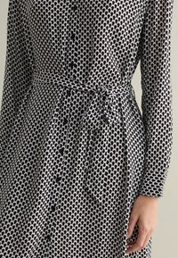 Black and white patterned dress with a button-down front, long sleeves, and a tied waist belt. Features rounded shapes in the print.