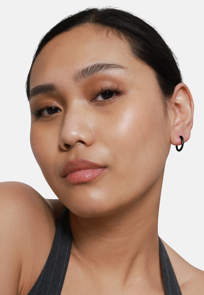 Svart hoop øredobbe brukt på høyre øre. Glatt metallfinish, sirkulær form, og et minimalistisk design som komplementerer det totale utseendet.