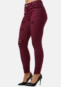 Vaqueros skinny burdeos con detalles desgastados en los muslos y dobladillos deshilachados. Confeccionados con un tejido elástico para un ajuste ceñido.
