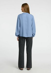 Ljusblå långärmad blus med ett subtilt prickmönster, rundad nederkant och ballongärmar, ihop med högmidjade mörka denimbyxor.