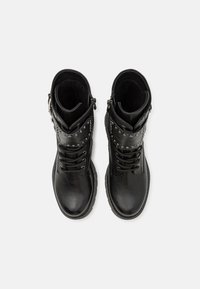 Botas de tobillo de cuero negro con una textura suave, cordones y tachuelas de plata decorativas en la parte superior. Cuentan con una cremallera lateral para facilitar su uso.