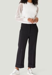 Pull blanc avec des manches longues en maille texturée, pantalon noir à jambe large avec des poignets retournés, et chaussures de sport argentées.
